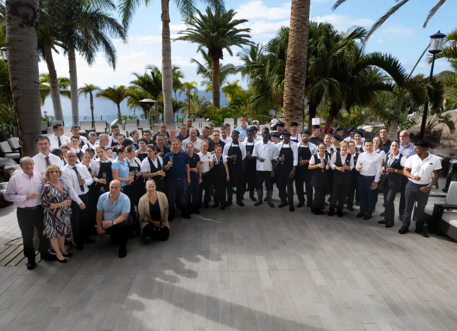 Grupo de personas con uniforme posando al aire libre, rodeados de palmeras y mar.