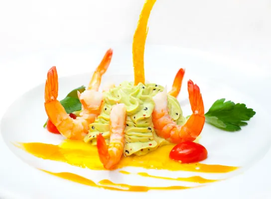 Camarones con puré verde, tomates cherry y salsa amarilla en un plato decorado.