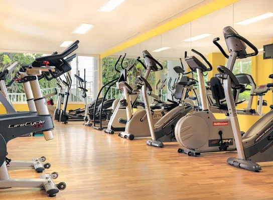 Gimnasio con bicicletas estáticas alineadas frente a un espejo en una sala con piso de madera.