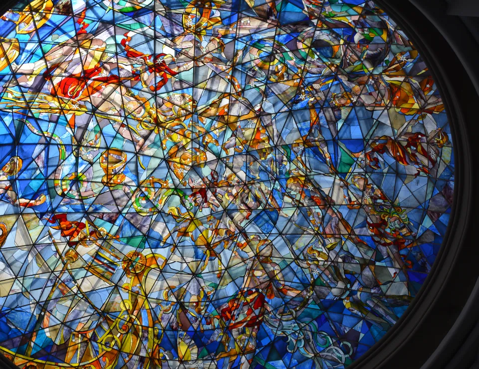 Vidriera circular con figuras y colores vibrantes en tonos azules, amarillos y rojos.