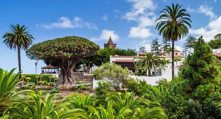 Paisaje tropical con vegetación exuberante y arquitectura colonial bajo un cielo azul.