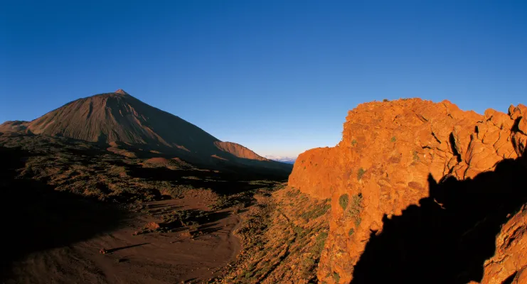 Montaña con pendiente rocosa a la derecha, cielo despejado al fondo.