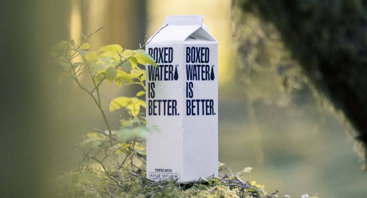 Cartón de agua "Boxed Water" en un entorno natural con vegetación.