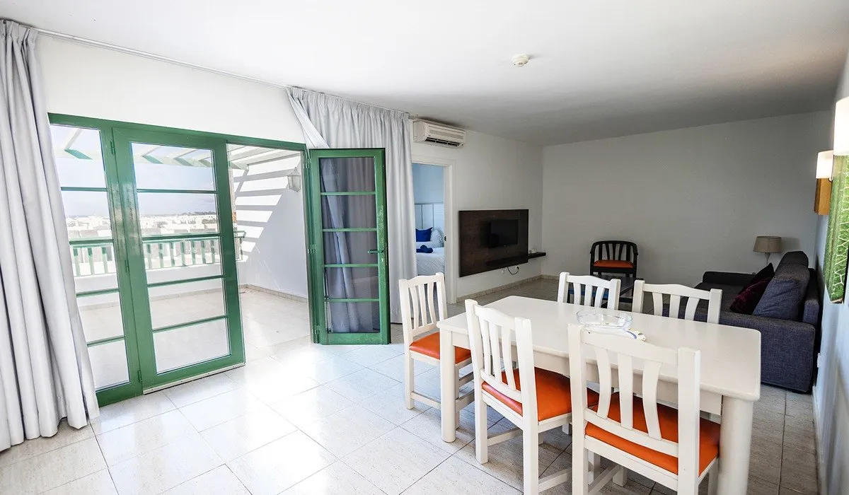 Sala-comedor luminosa con mesa blanca y puertas de balcón verde.