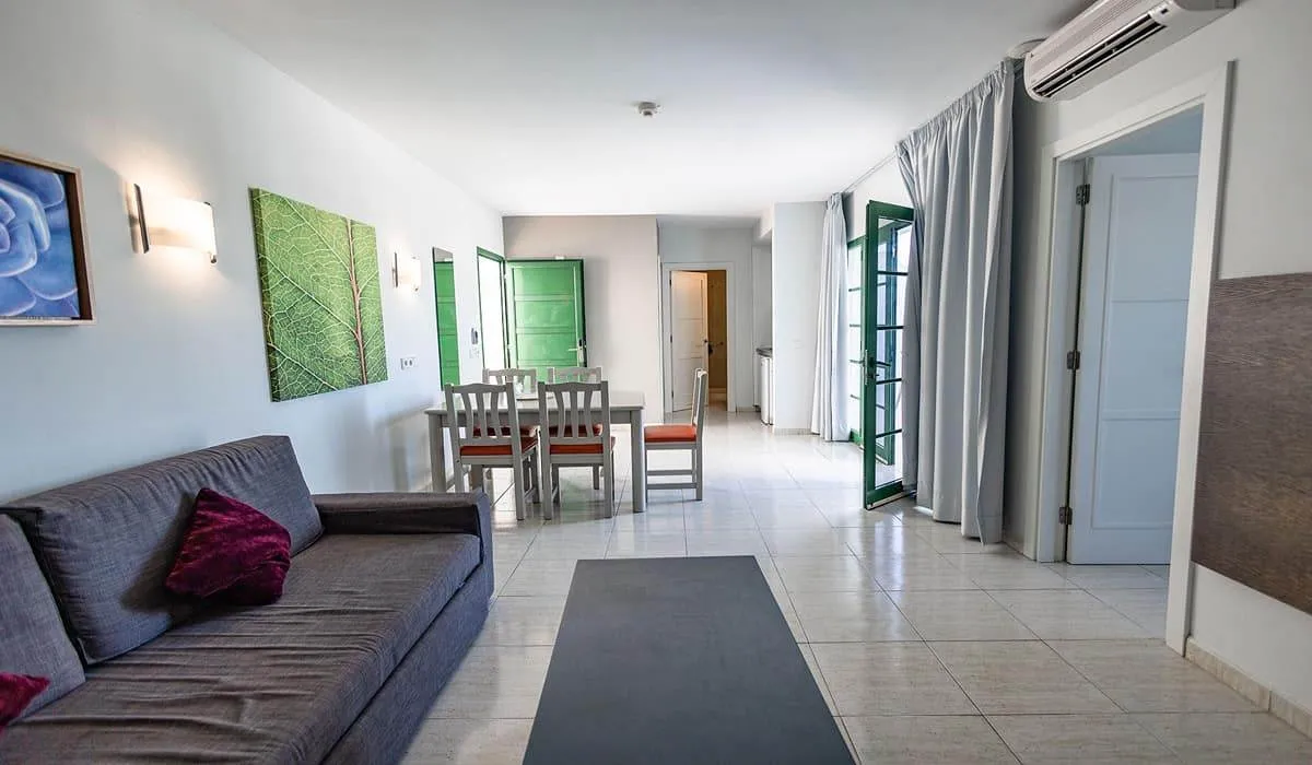 Sala de estar con sofá, mesa de comedor, y puertas verdes iluminadas.