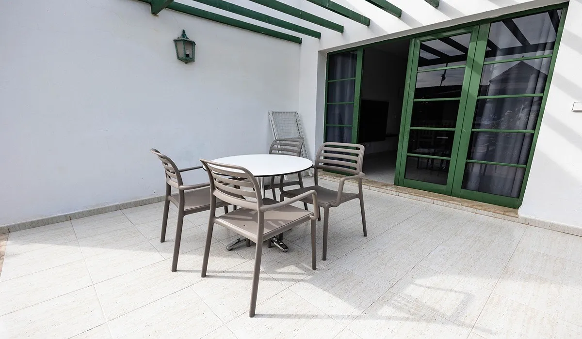 Patio con mesa redonda, cuatro sillas y puerta corredera verde.