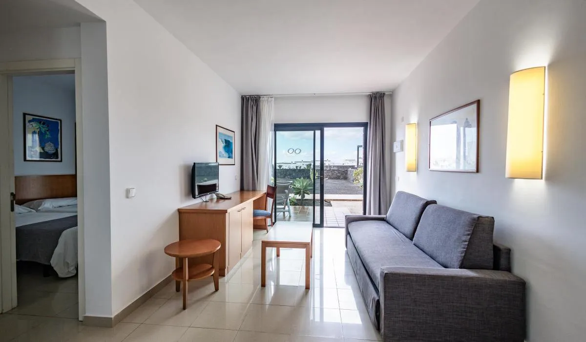 Sala moderna con sofá, mesa y televisión, vista a terraza a través de puertas de cristal.