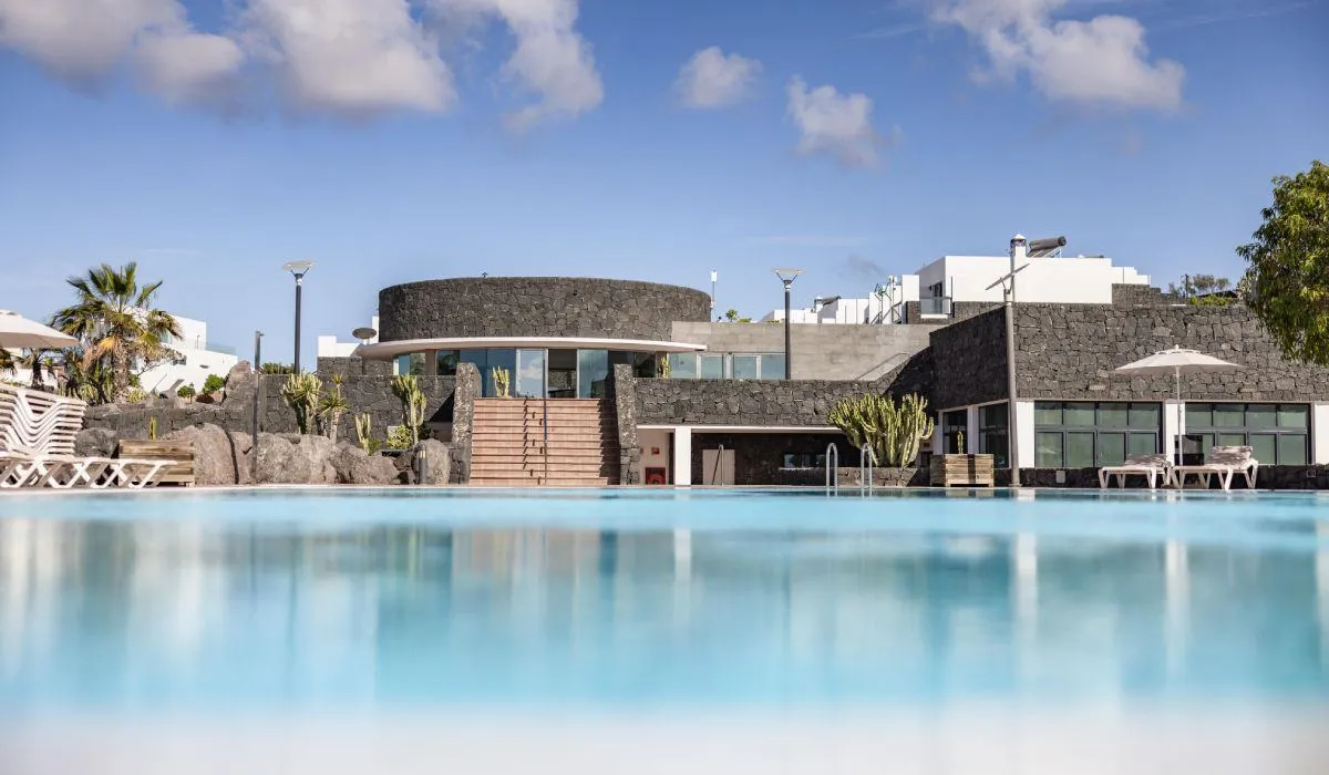 Piscina con una moderna casa de piedra detrás y cielo azul.