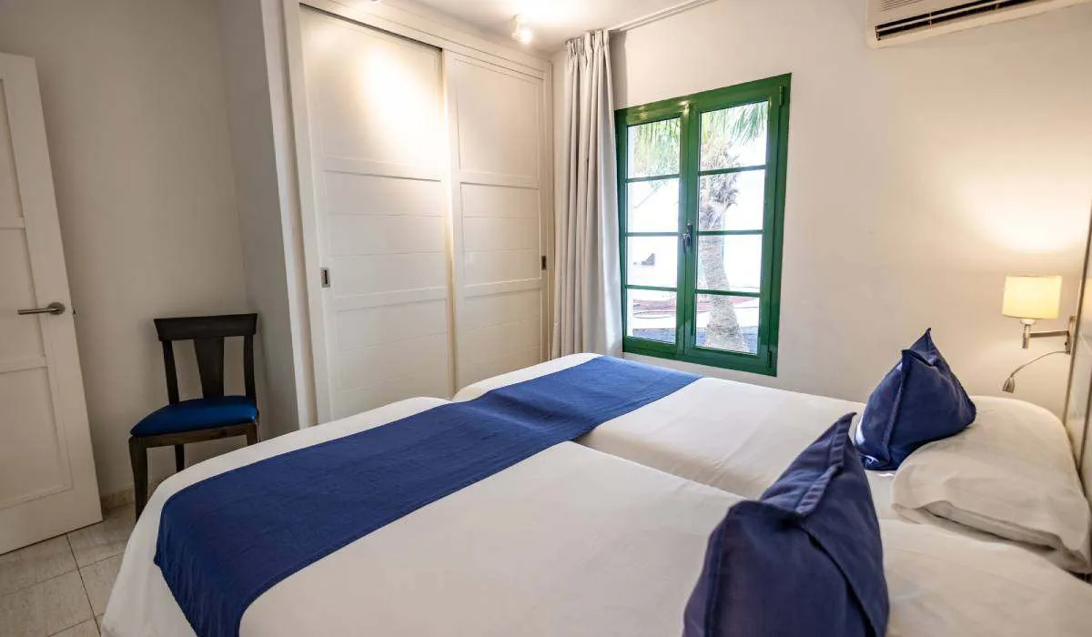 Habitación con dos camas, ventanas verdes y decoración en azul.