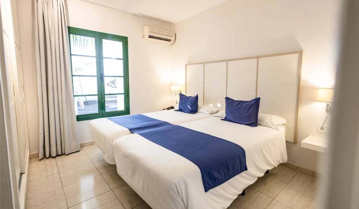 Dos camas con almohadas azules en una habitación luminosa.