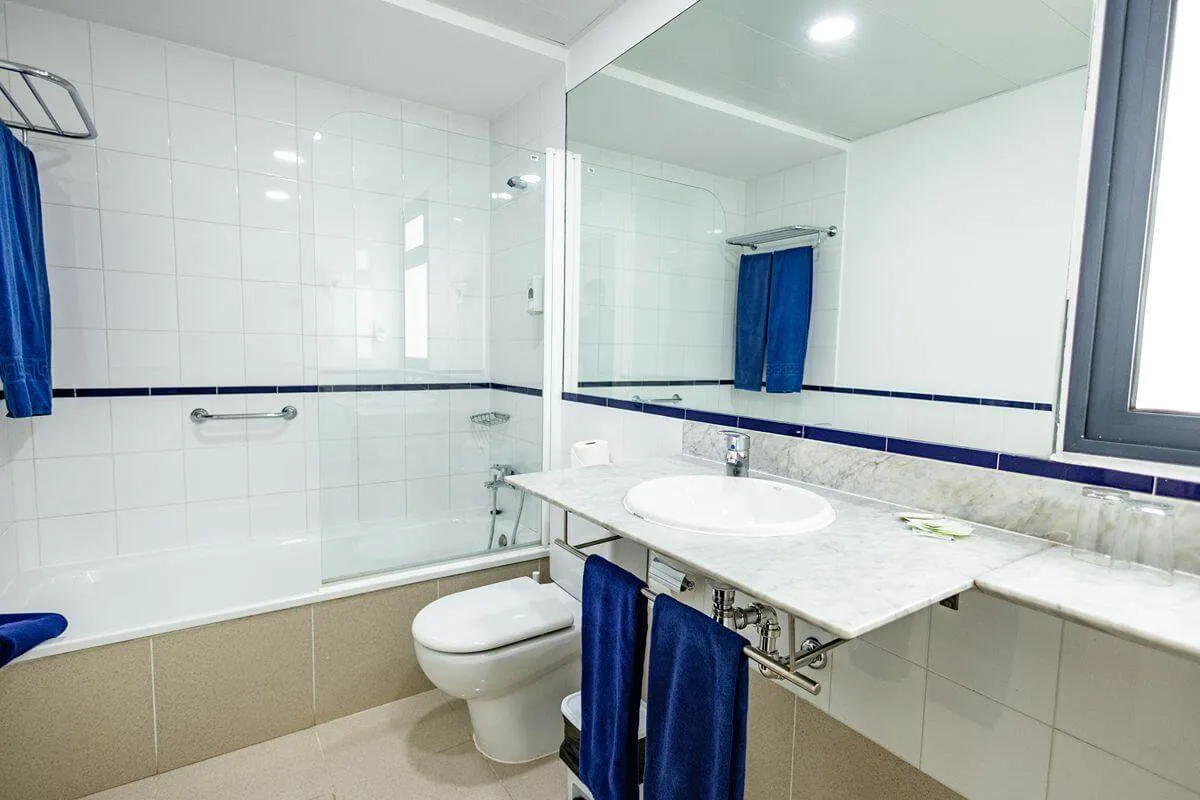 Baño moderno con azulejos blancos, espejo, lavabo y toallas azules.