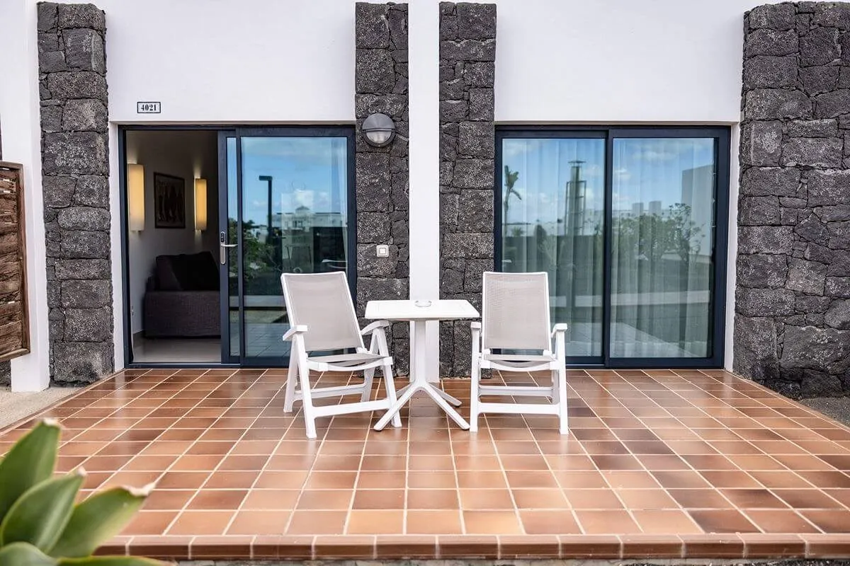 Terraza con dos sillas y mesa frente a una puerta corredera de cristal.