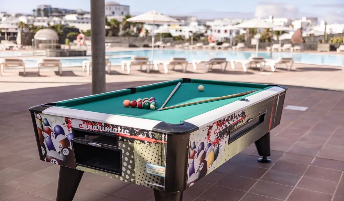 Mesa de billar junto a una piscina en un hotel, con bolas y tacos listos.