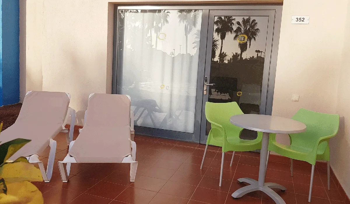 Terraza con dos tumbonas, mesa y sillas junto a puerta corredera.