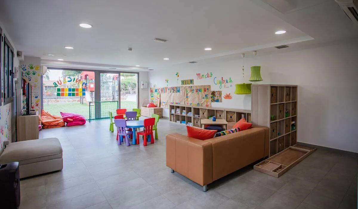 Sala de juegos infantil con mesas y sillas coloridas, sofás y decoración alegre.