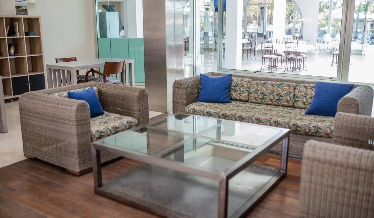 Sala de estar con sofás de mimbre, cojines azules y mesa de vidrio.