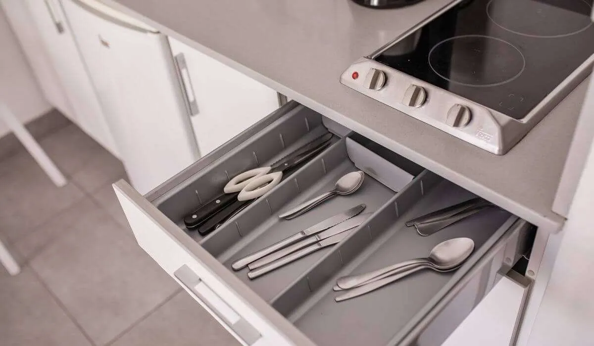 Cajón de cubiertos abierto en la cocina junto a una estufa eléctrica.