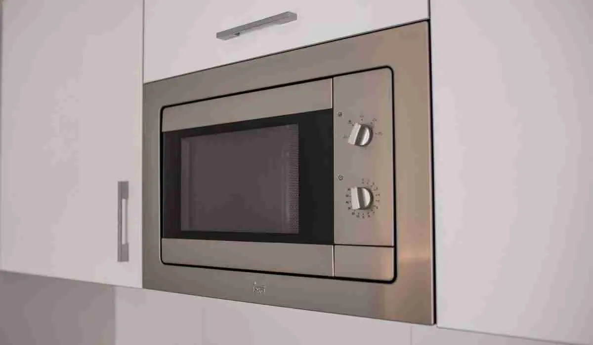 Microondas empotrado en gabinete blanco con controles de perilla plateados.