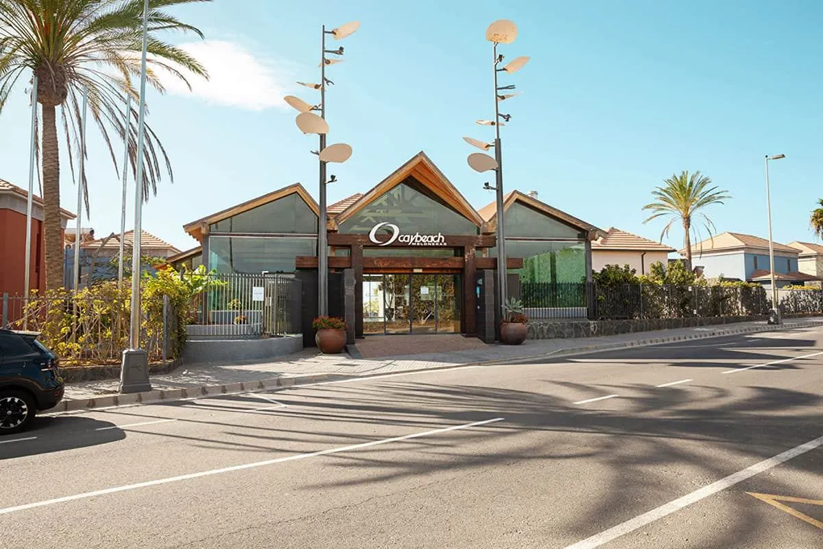 Entrada de un edificio moderno rodeado de palmeras y cielo azul.