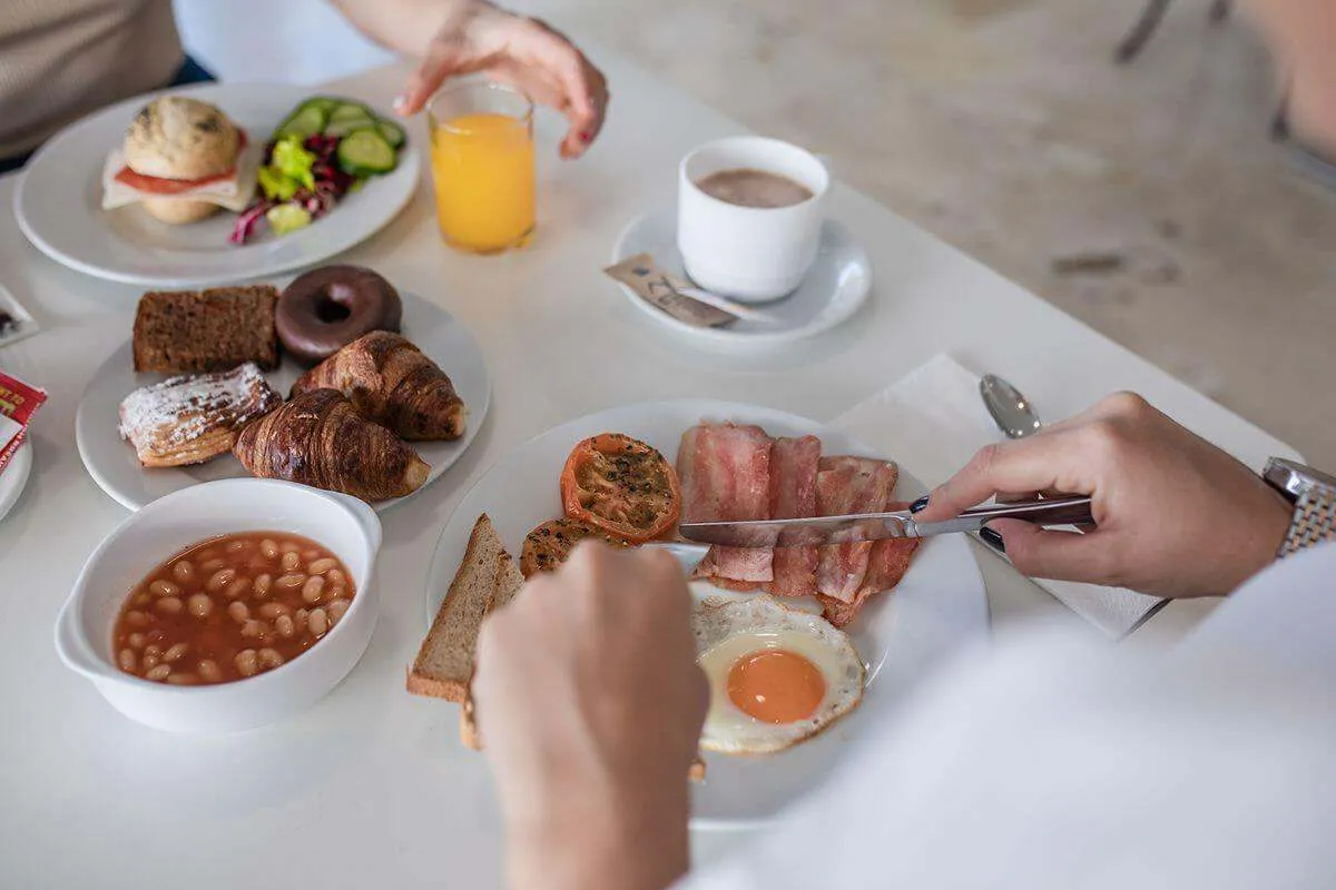 Desayuno variado con huevos, tocino, panes, café y jugo de naranja.