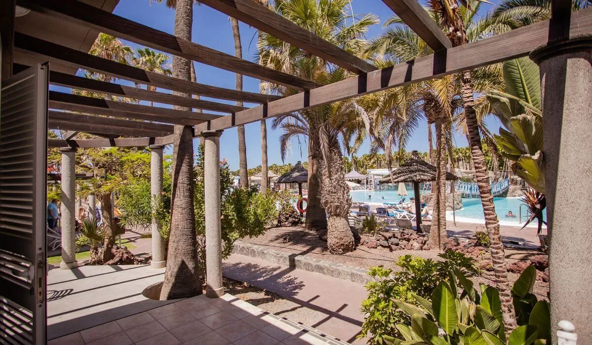 Pergola junto a piscina y palmeras en ambiente tropical y soleado.