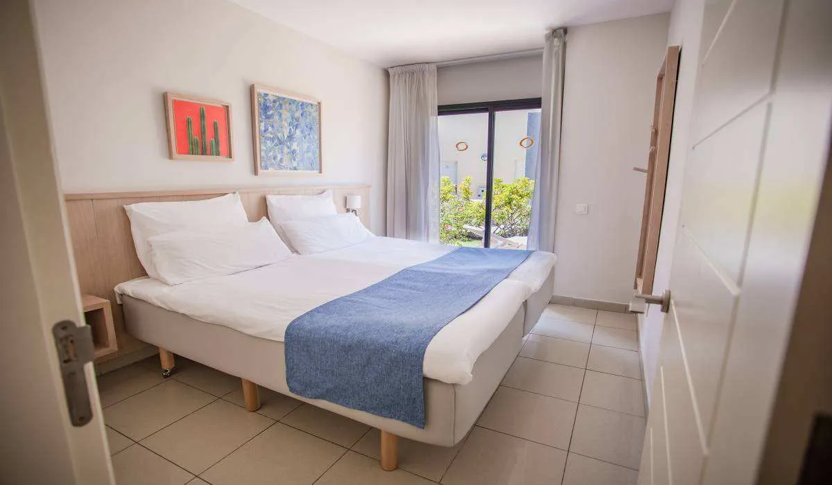 Habitación luminosa con cama doble, cuadros y ventanal con vista al jardín.