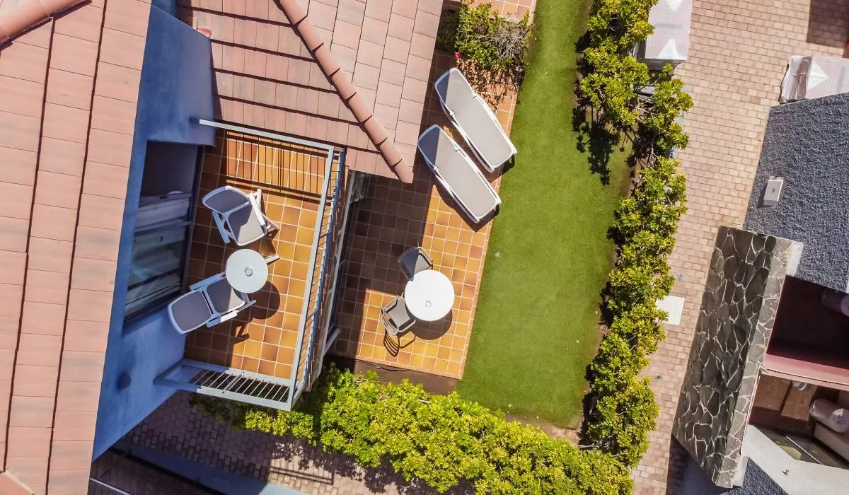 Vista aérea de terraza con mesas, sillas y césped rodeada de plantas.