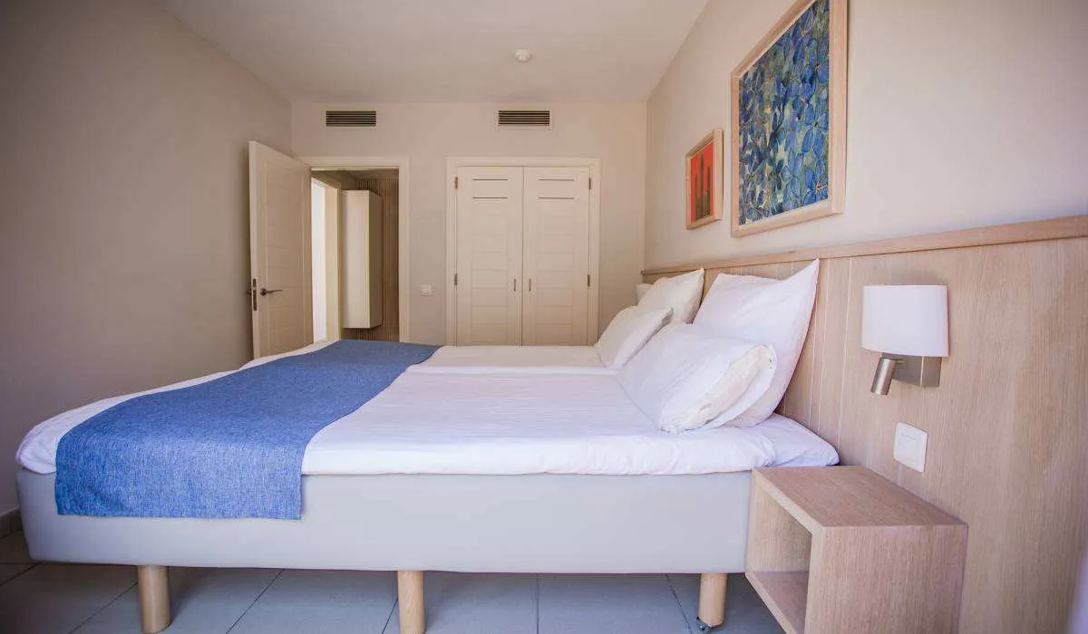 Cama doble en habitación minimalista con cuadros y puerta entreabierta.