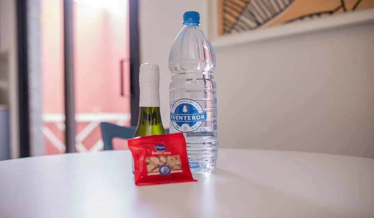 Botella de agua, botella de vino y paquete de frutos secos en una mesa blanca.