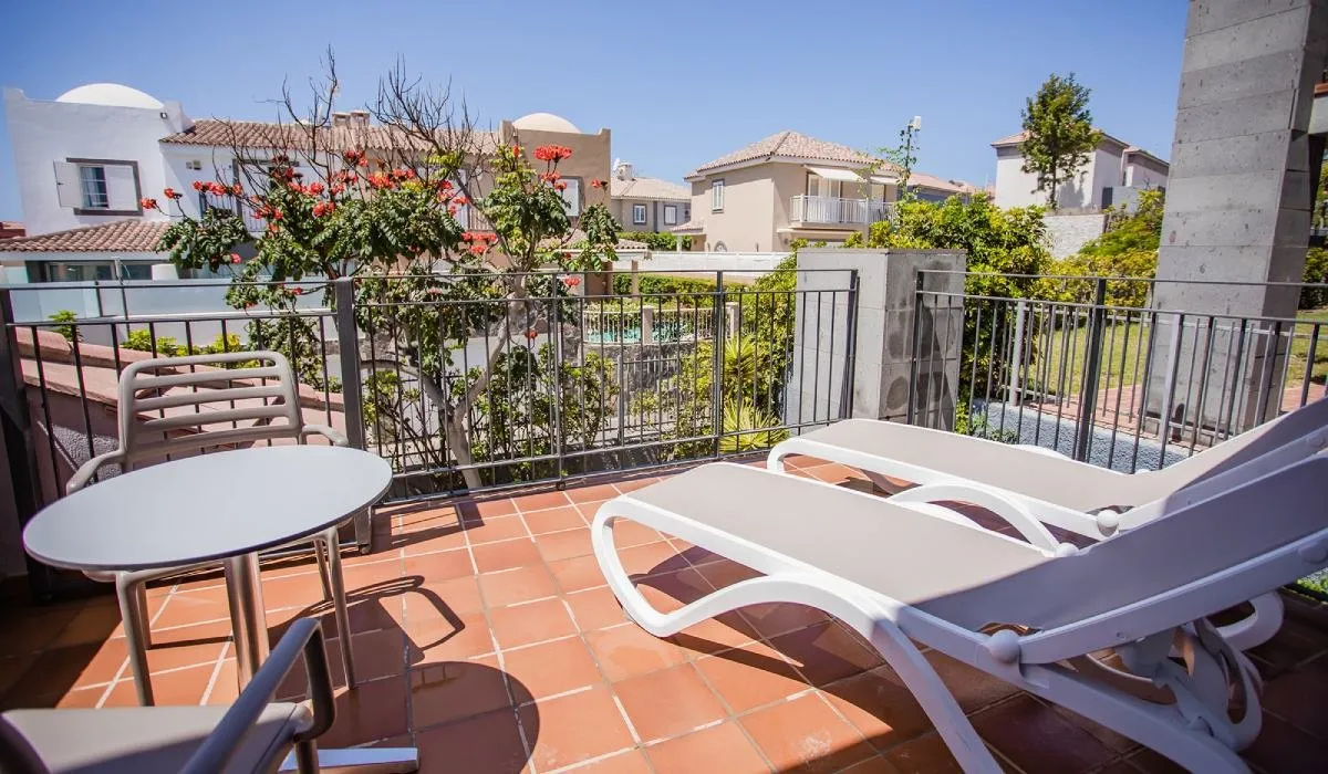 Terraza con tumbonas y vista a un jardín, rodeada de edificios.