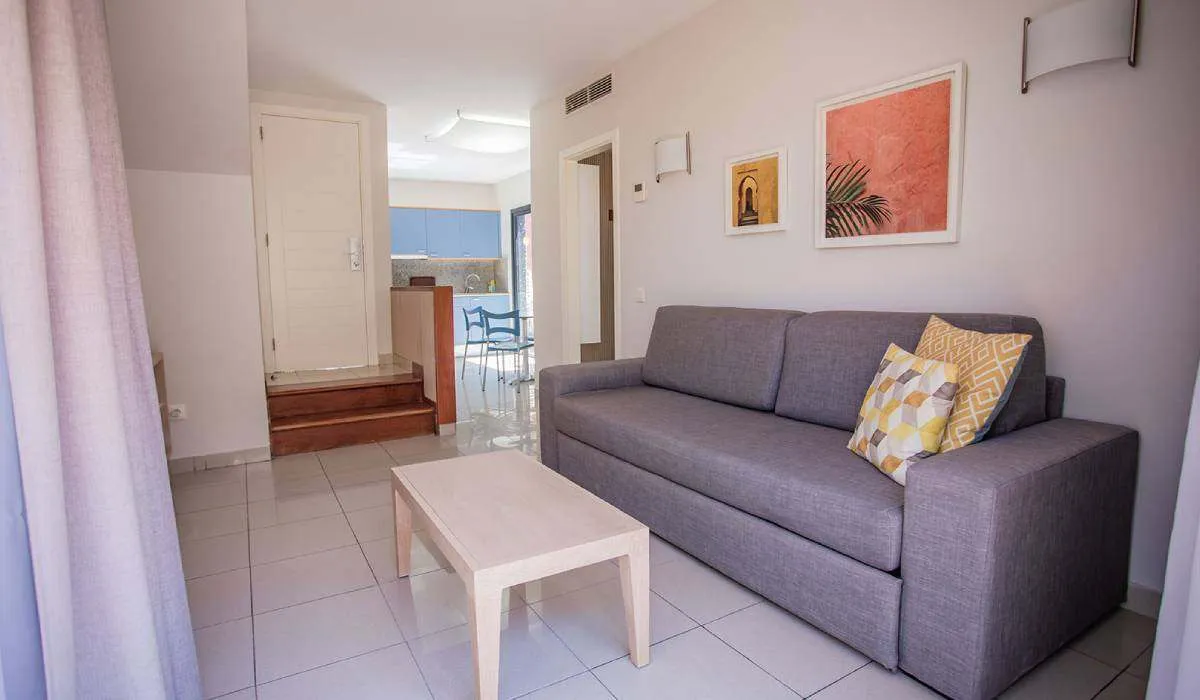 Sala moderna con sofá gris, cojines coloridos y mesa de centro de madera clara.