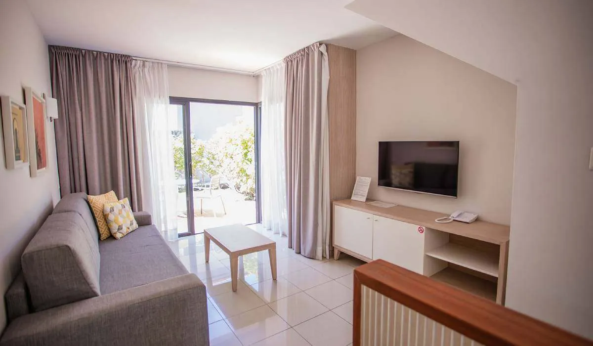 Sala moderna con sofá gris, mesa, TV y vista al exterior.