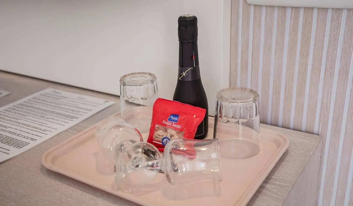 Botella, vaso y frutos secos sobre bandeja clara de madera.