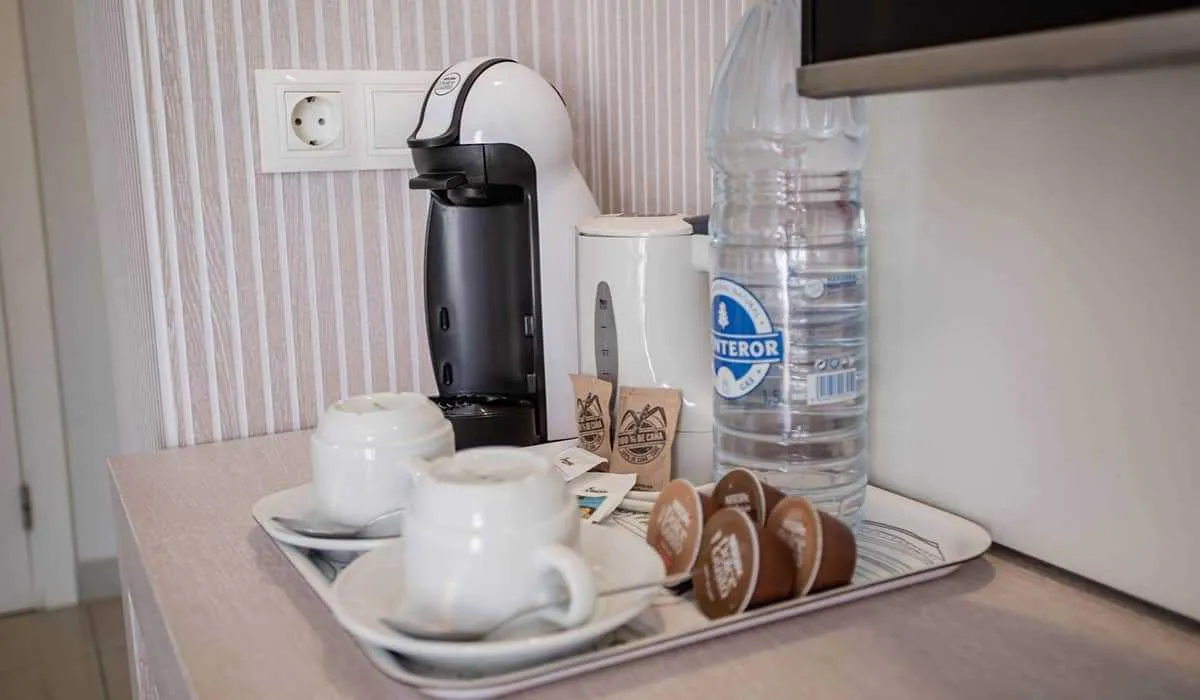 Cafetera, tazas, cápsulas y botella de agua sobre una bandeja en una mesa.