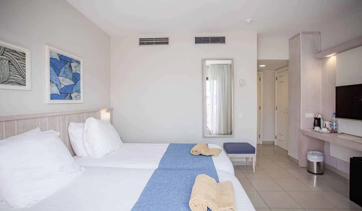 Habitación de hotel moderna con dos camas, arte, televisor y baño al fondo.