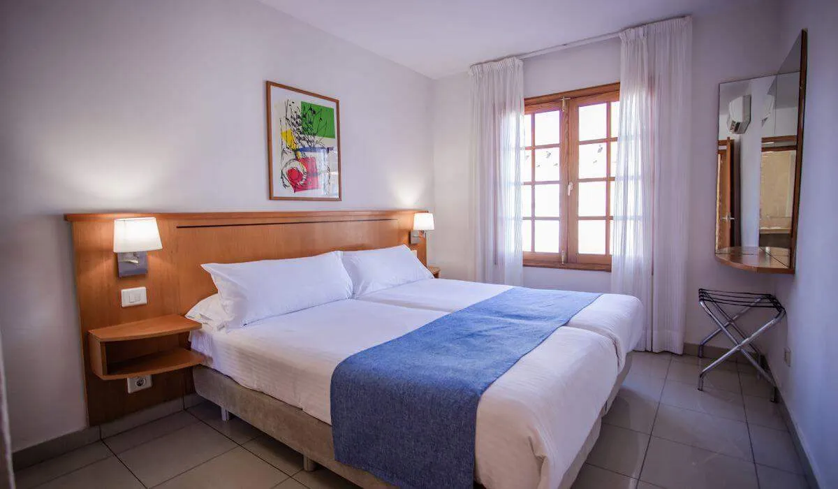 Habitación de hotel con cama doble y ventana iluminada por luz natural.