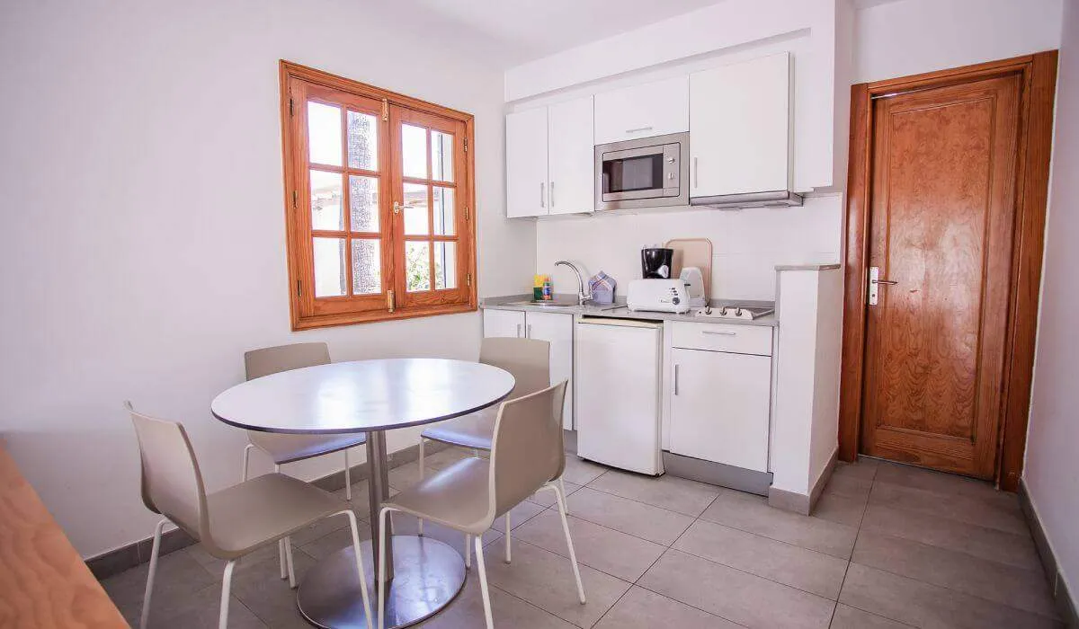 Cocina blanca con mesa redonda, sillas, ventana de madera y puerta de madera.