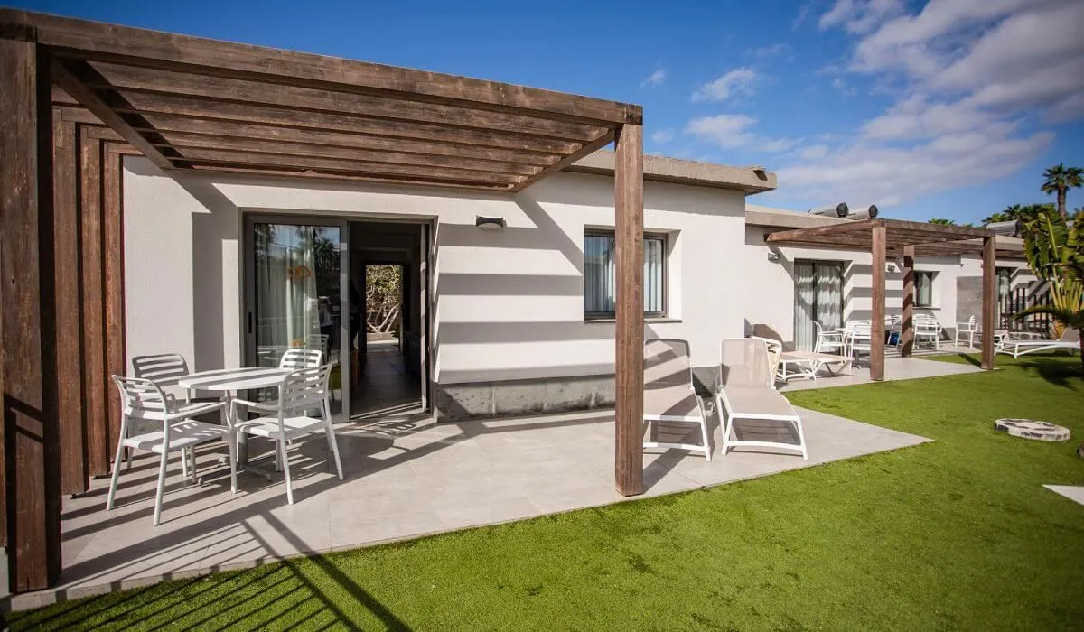 Casa moderna con pérgola, sillas y mesas en un patio soleado.