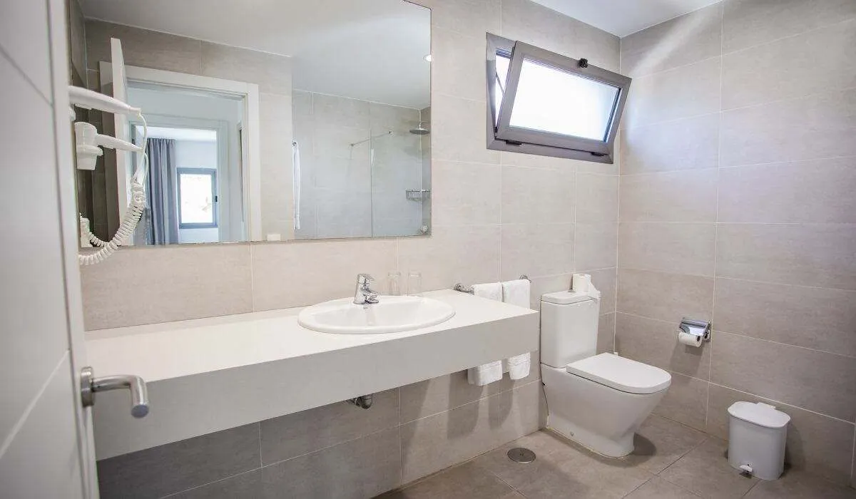 Baño moderno con lavabo, espejo, inodoro y ventana pequeña abierta.