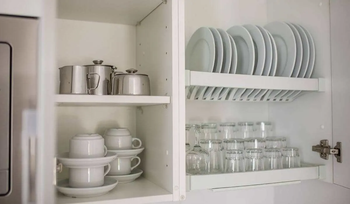 Estantes de cocina con platos, tazas y cristalería organizada.