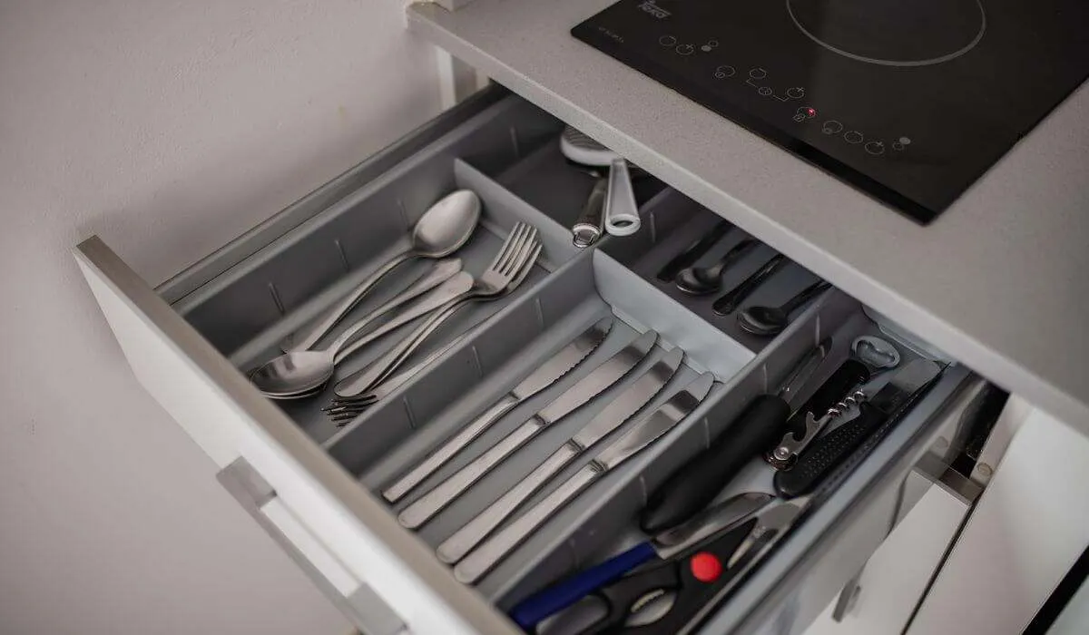 Cajón abierto con cubiertos y utensilios de cocina ordenados.