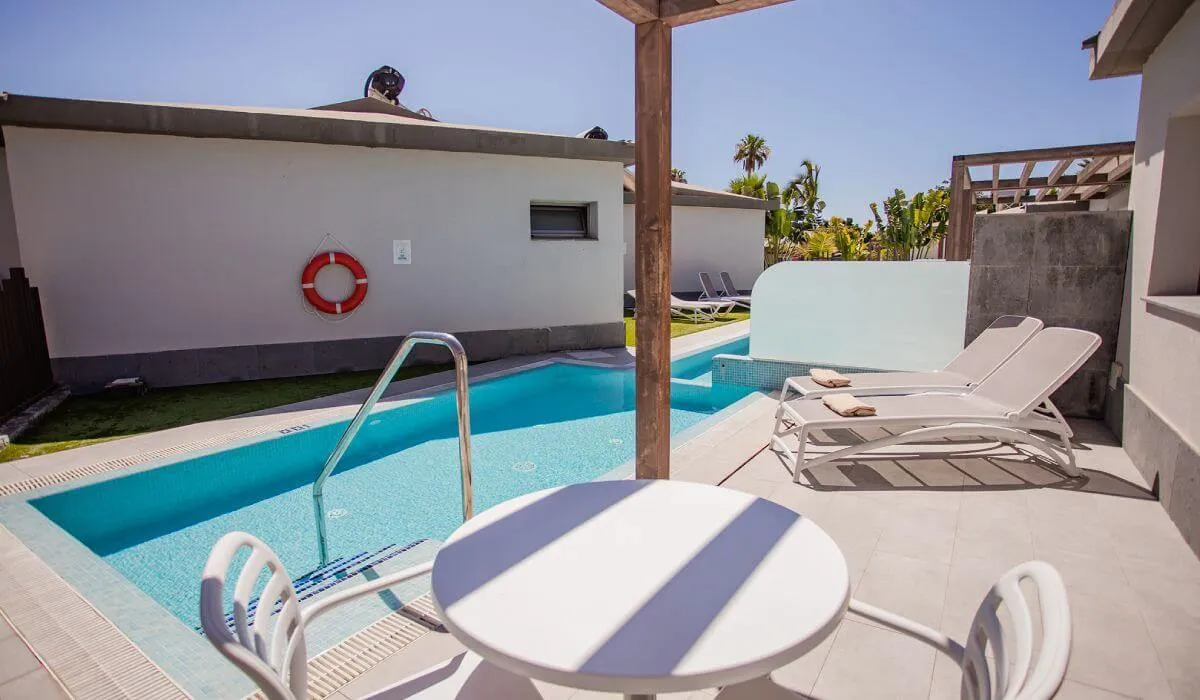 Piscina con tumbonas y mesa de exterior en un día soleado.