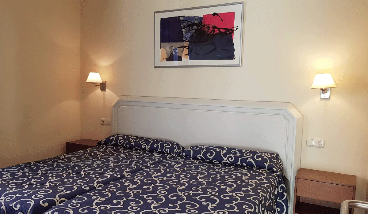 Habitación de hotel con cama doble, lámparas y un cuadro en la pared.