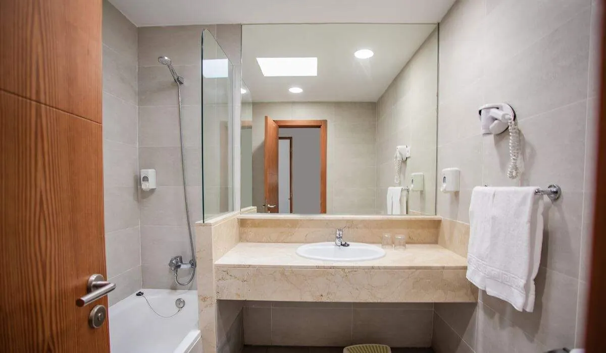 Baño moderno con lavabo, espejo, secador y bañera blanca.