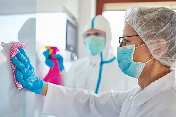 Personas en equipo protector limpiando una superficie con esponja y spray.