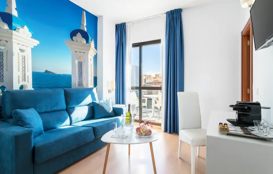Sala luminosa con sofá azul, ventana y decoración de paisaje marítimo.
