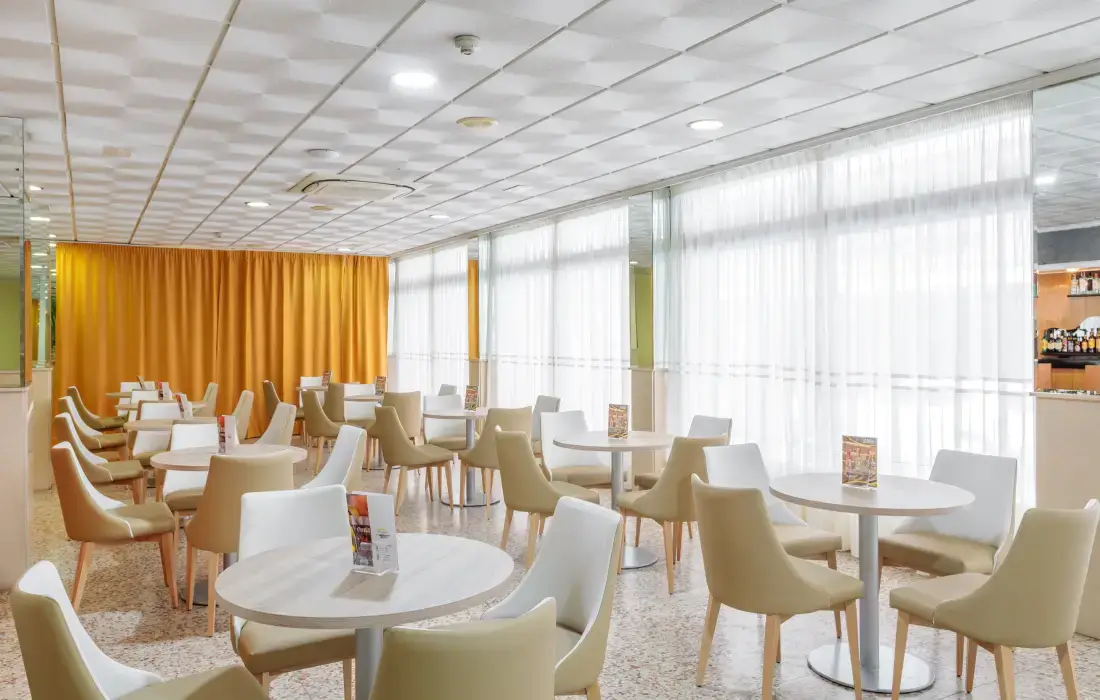 Sala de estar con sillas claras, mesas redondas y cortinas amarillas.