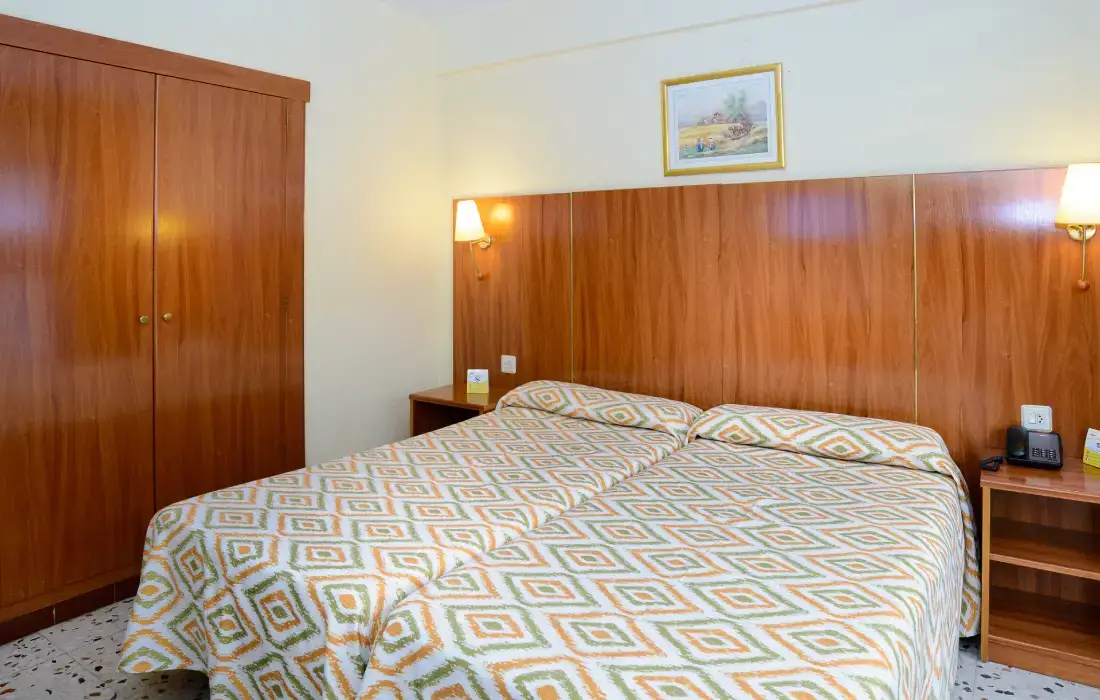 Cama doble con colcha geométrica en habitación de hotel.