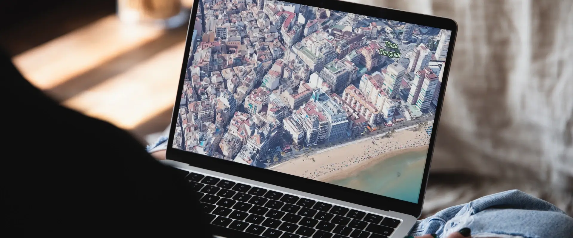 Pantalla de laptop mostrando vista a&eacute;rea de una ciudad costera.