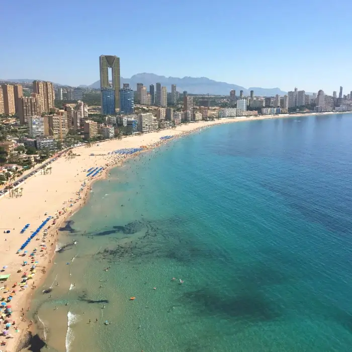 Vista de una playa concurrida y rascacielos al fondo bajo un cielo despejado.